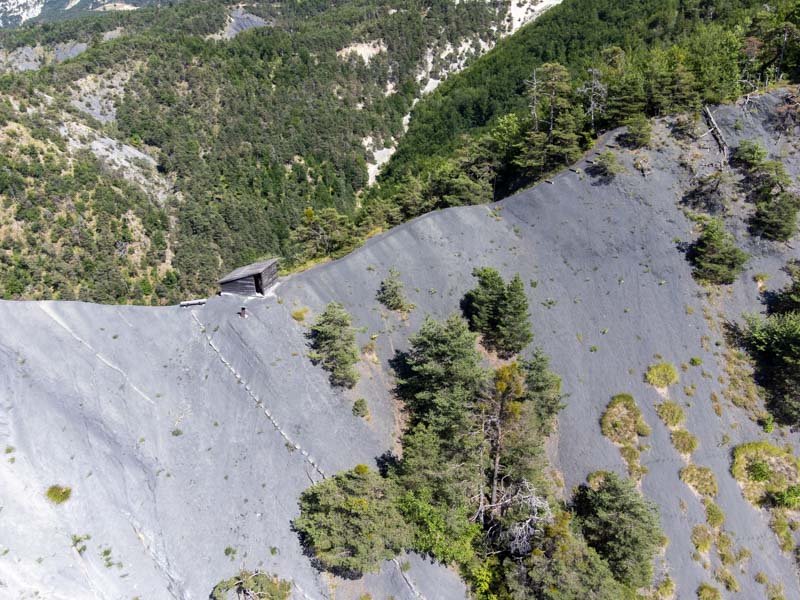 Vue arienne du site de l'ichtyosaure de La Mlaie  Prads-Haute-Blone, montrant la cabane en bois protgeant le fossile, situe sur une pente de marnes grises entoure de forts et de montagnes.