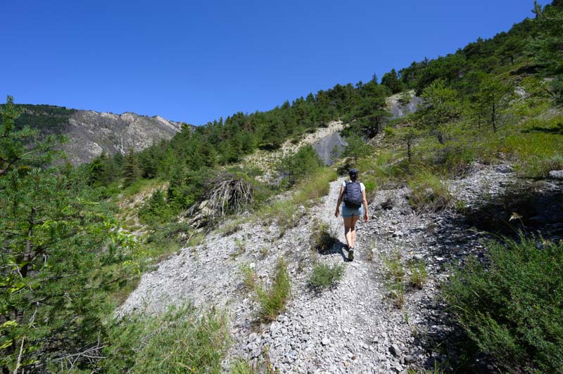 Randonne sur le sentier menant au site de l'ichtyosaure de La Mlaie  Prads-Haute-Blone, avec une randonneuse traversant un paysage montagneux parsem de vgtation sous un ciel bleu.